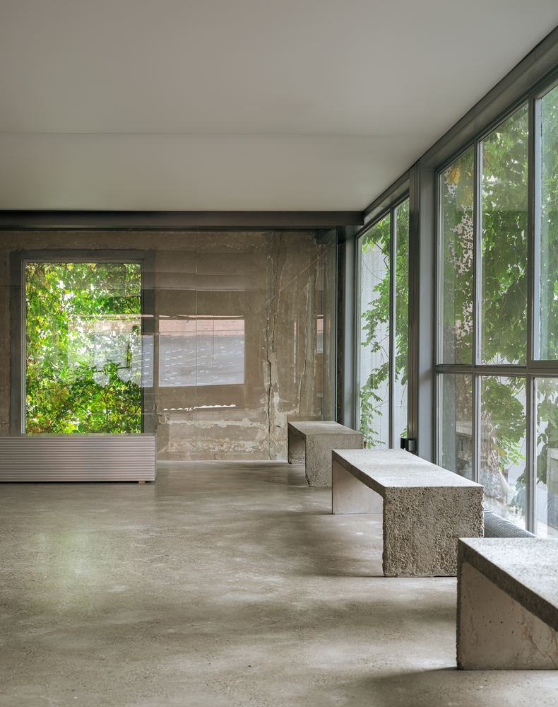 Concrete stepped seating beside floor-to-ceiling windows with foliage visible outside in daylight
