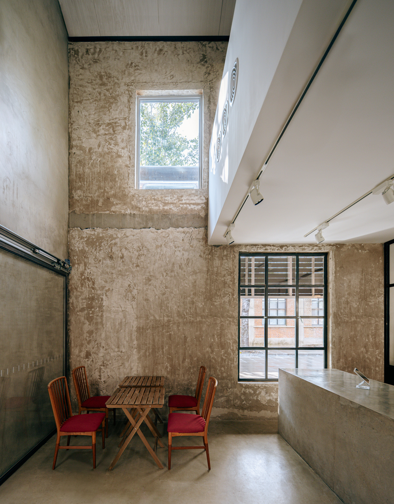 Double-height dining area with exposed plaster walls and wooden table beneath clerestory window