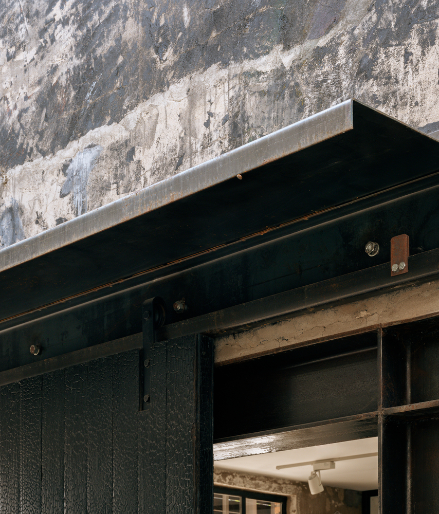 Black-stained timber sliding door with exposed steel track against weathered concrete wall