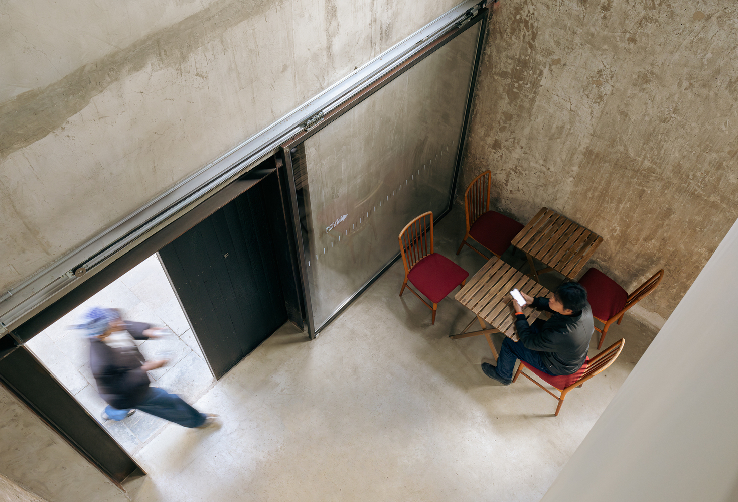 Overhead view of person seated at wooden table near entrance as visitors pass through doorway