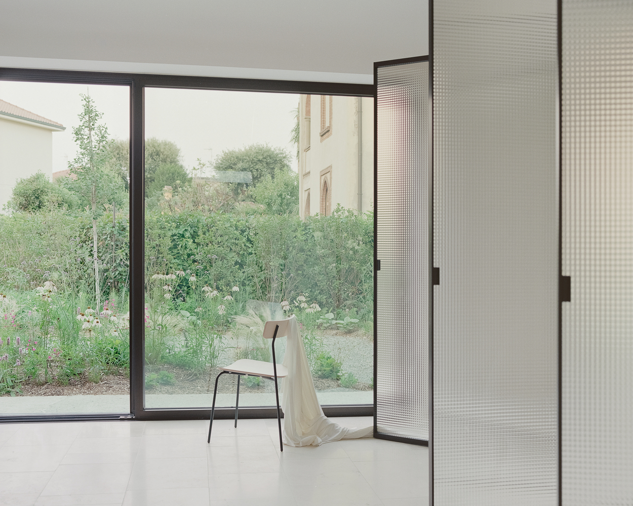Corner window overlooking a garden with a single chair draped in fabric on polished floor