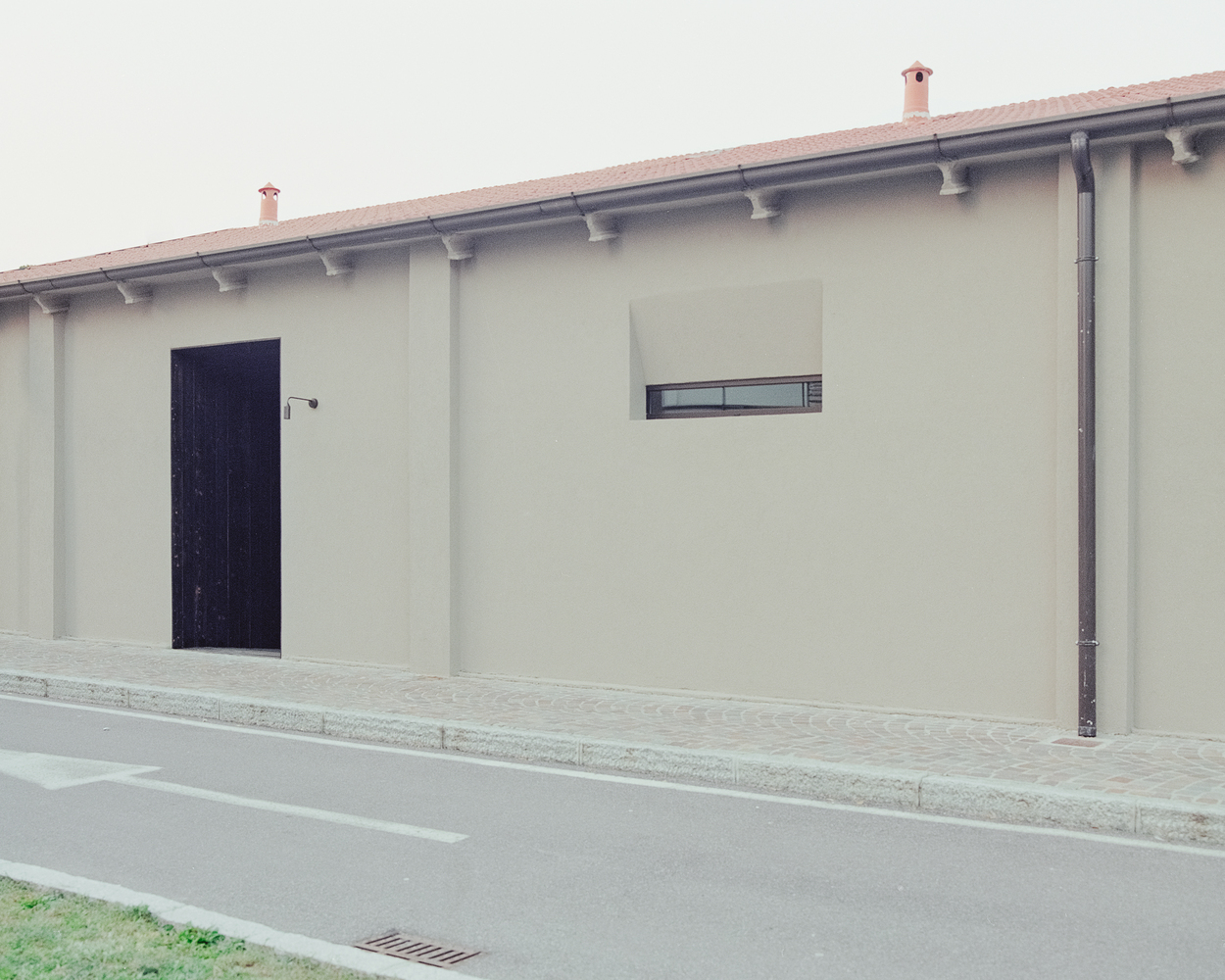 Street facade with recessed black timber door, narrow window and terracotta tile eaves under overcast sky