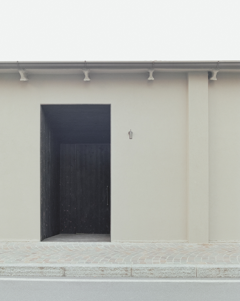 Black timber entry door set into smooth stucco wall with decorative terracotta corbels at the roofline