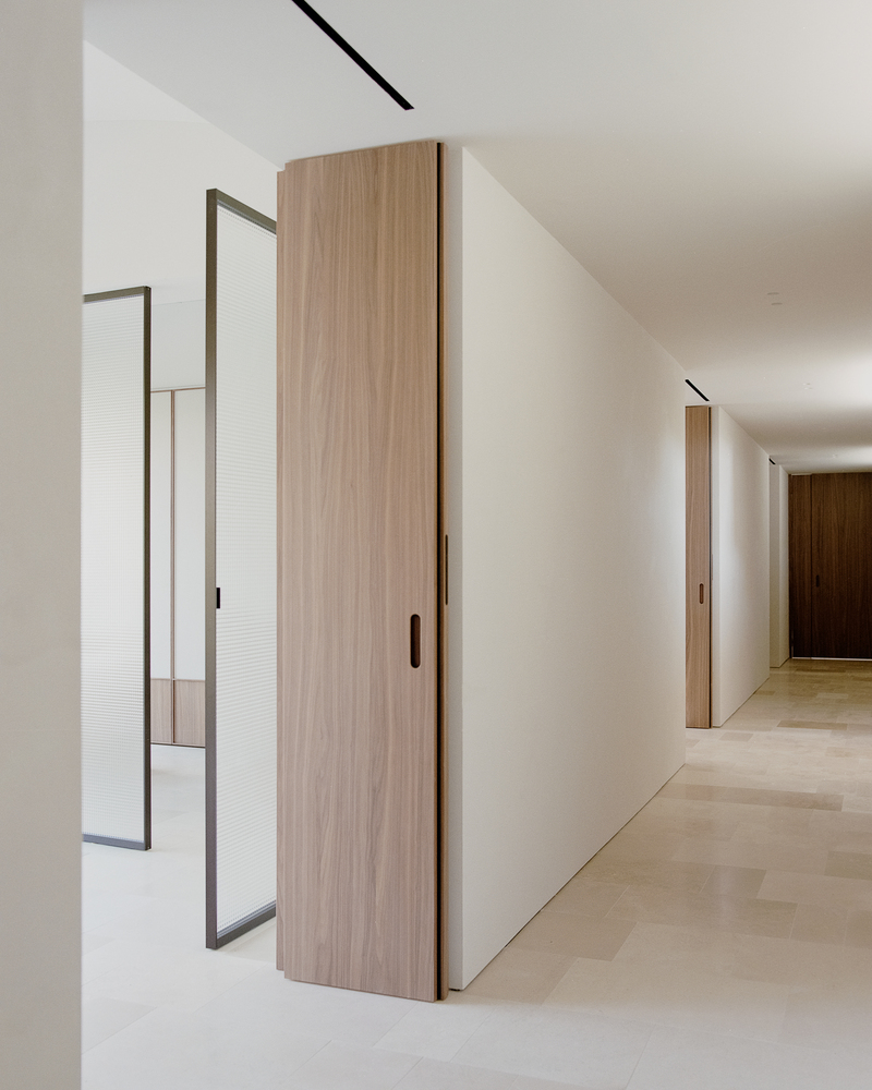 Corridor view showing walnut sliding doors, metal-framed reeded glass partition and recessed ceiling track