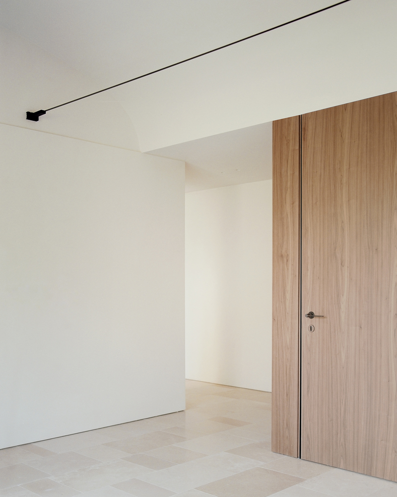 Interior corner with flush walnut door, white walls and linear black ceiling track lighting