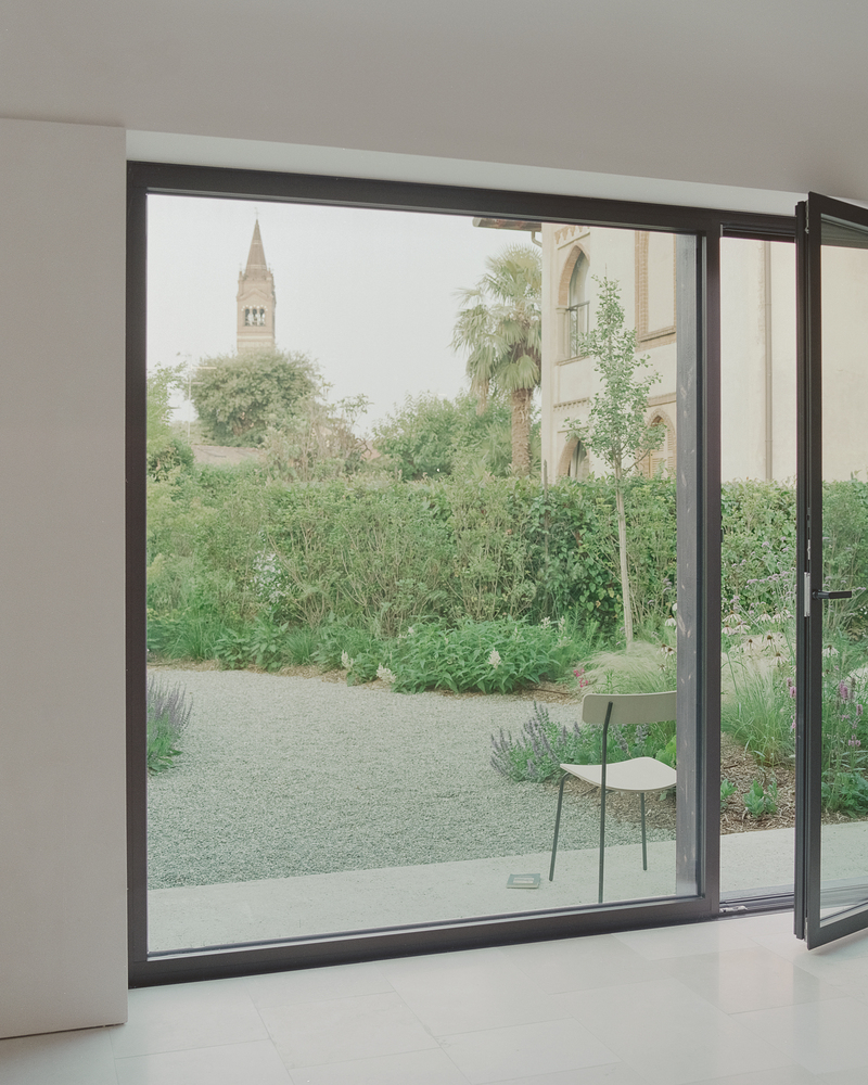 Open sliding glass door framing a view of a church bell tower beyond a garden path