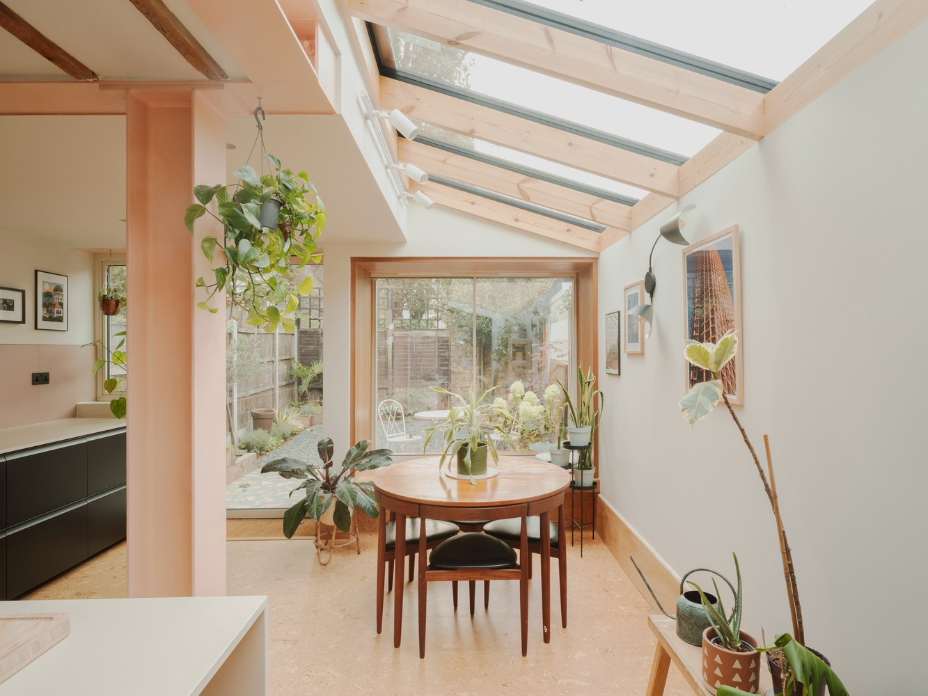 Dining area beneath exposed timber rafters and skylights with potted plants around a circular table