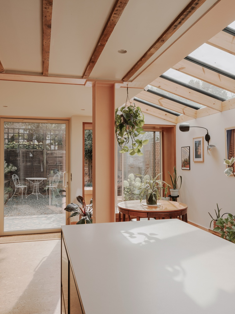 Kitchen island and dining table framed by timber columns with glazed doors opening to a gravel courtyard