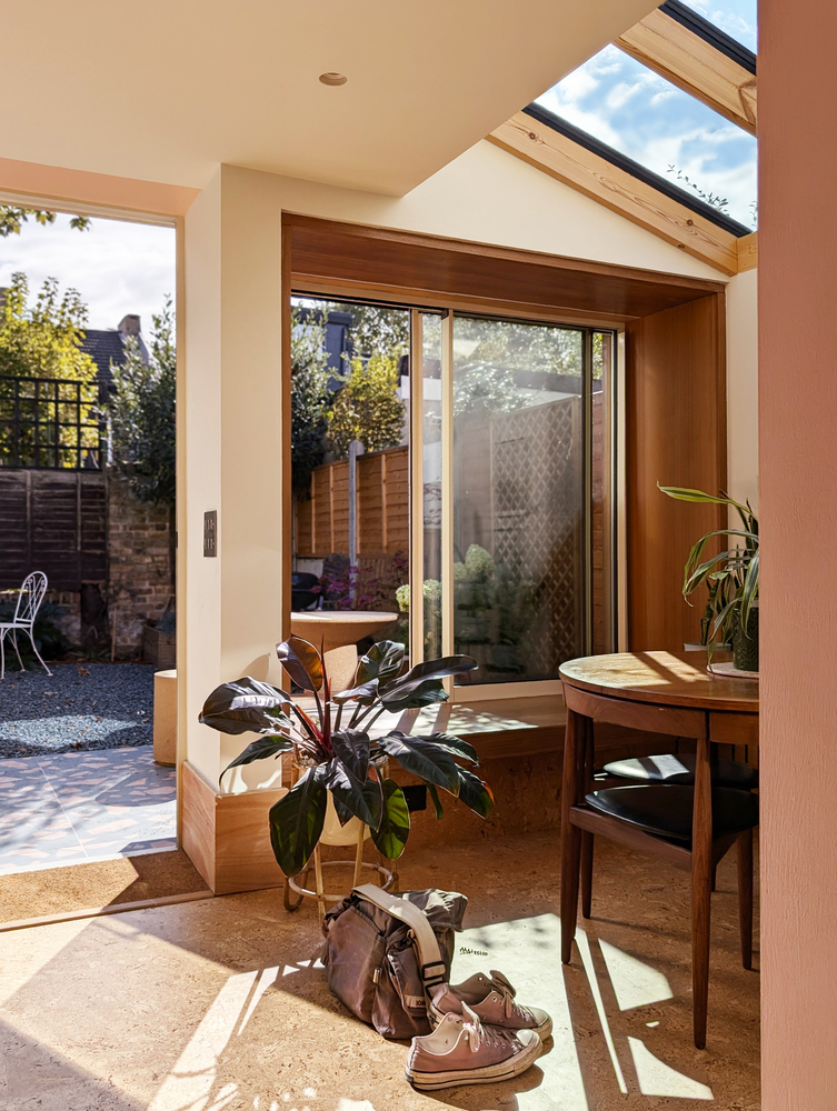 Interior corner with timber-framed bay window overlooking courtyard and morning sunlight on cork flooring