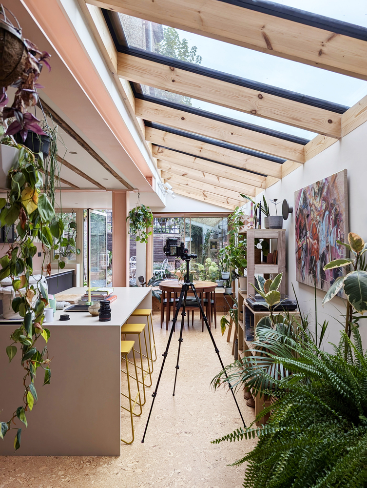 Open-plan kitchen and dining space with exposed timber rafters and abundant potted plants