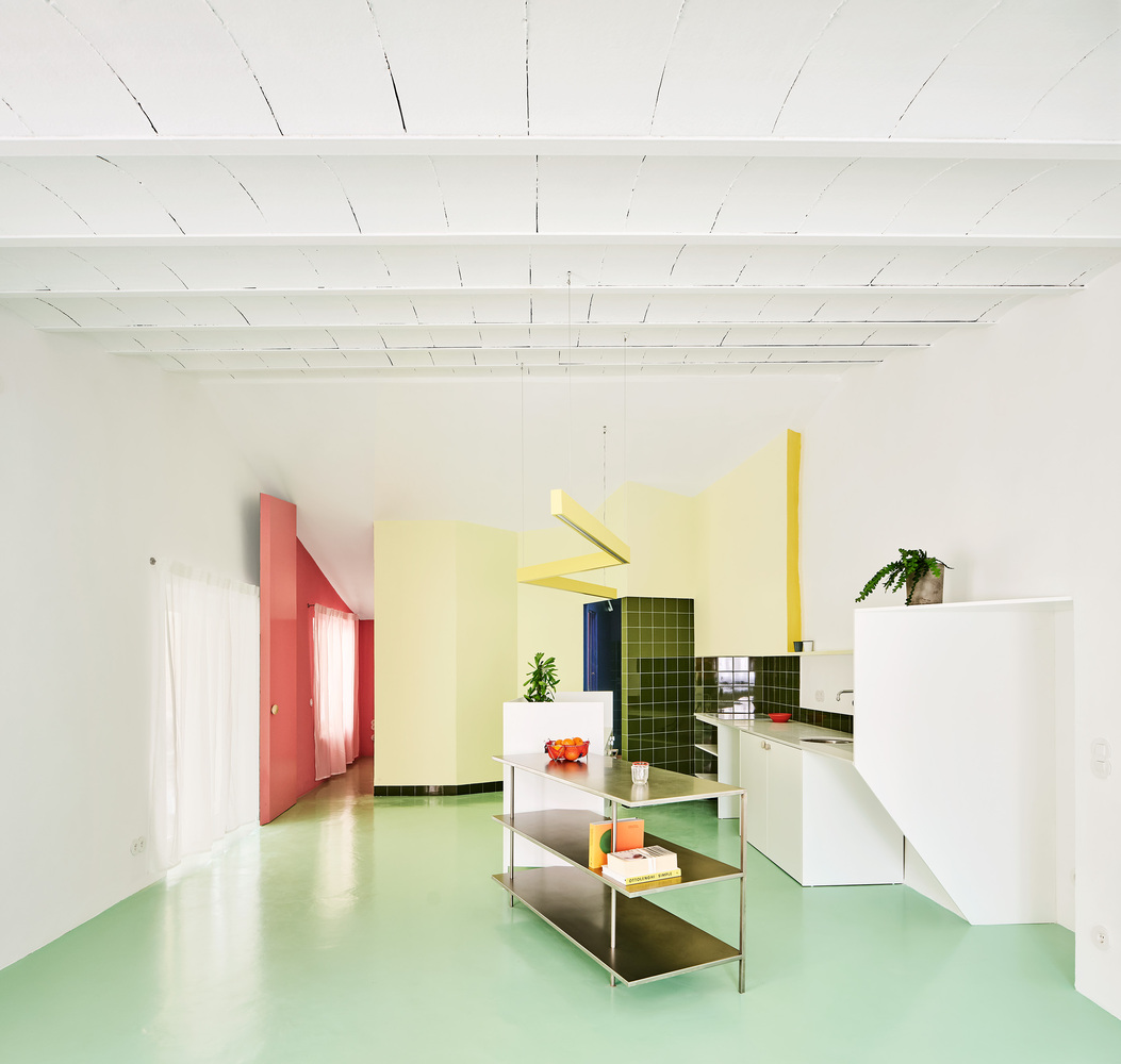 Open interior with pale green resin floor, white ceiling beams, and colorblocked partitions in pink and yellow