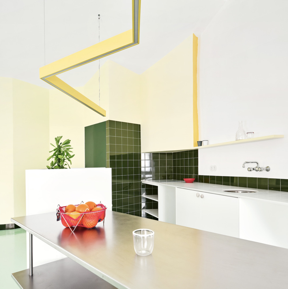Kitchen with dark green square tile backsplash, white countertops, and suspended yellow metal light fixture