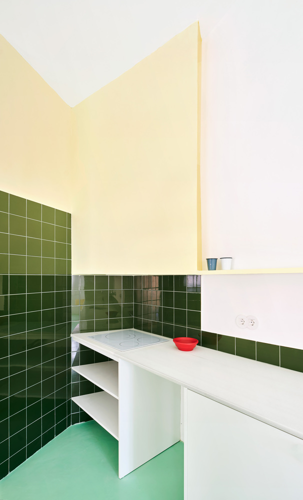 Kitchen corner with green tile walls, white base cabinets, and pale yellow partition above