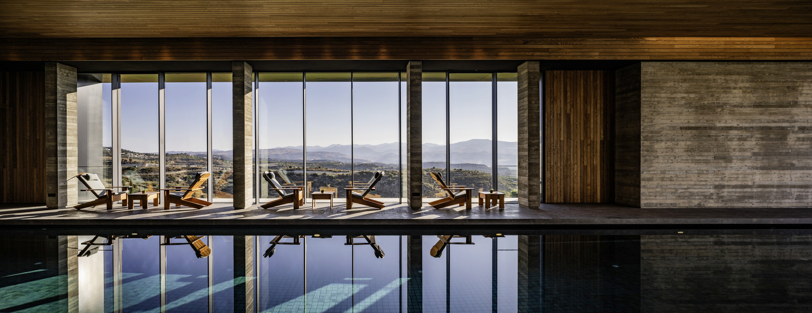 Indoor pool with floor-to-ceiling glazing overlooking distant hills and timber-clad ceiling