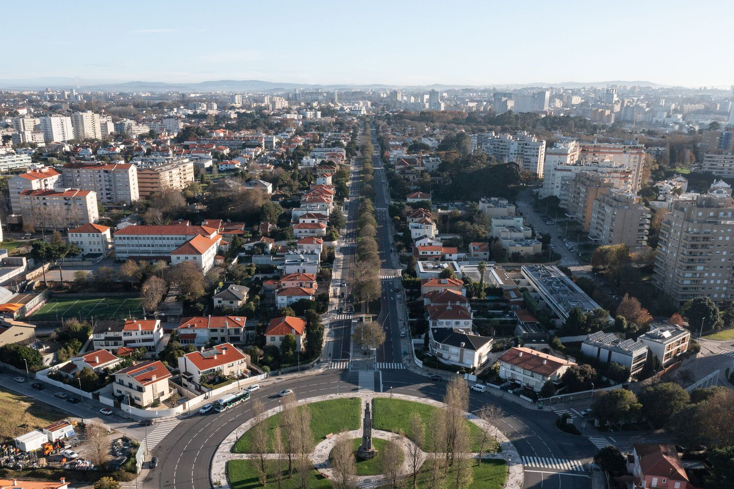 Wide aerial view of the urban neighborhood with the roundabout plaza and tree-lined streets