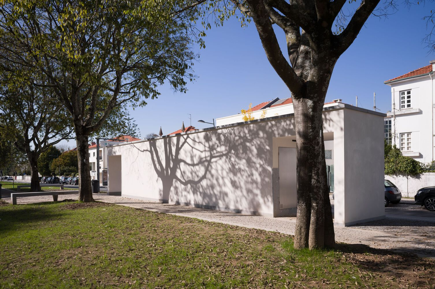 White pavilion structure casting tree shadows on its facade in the park setting