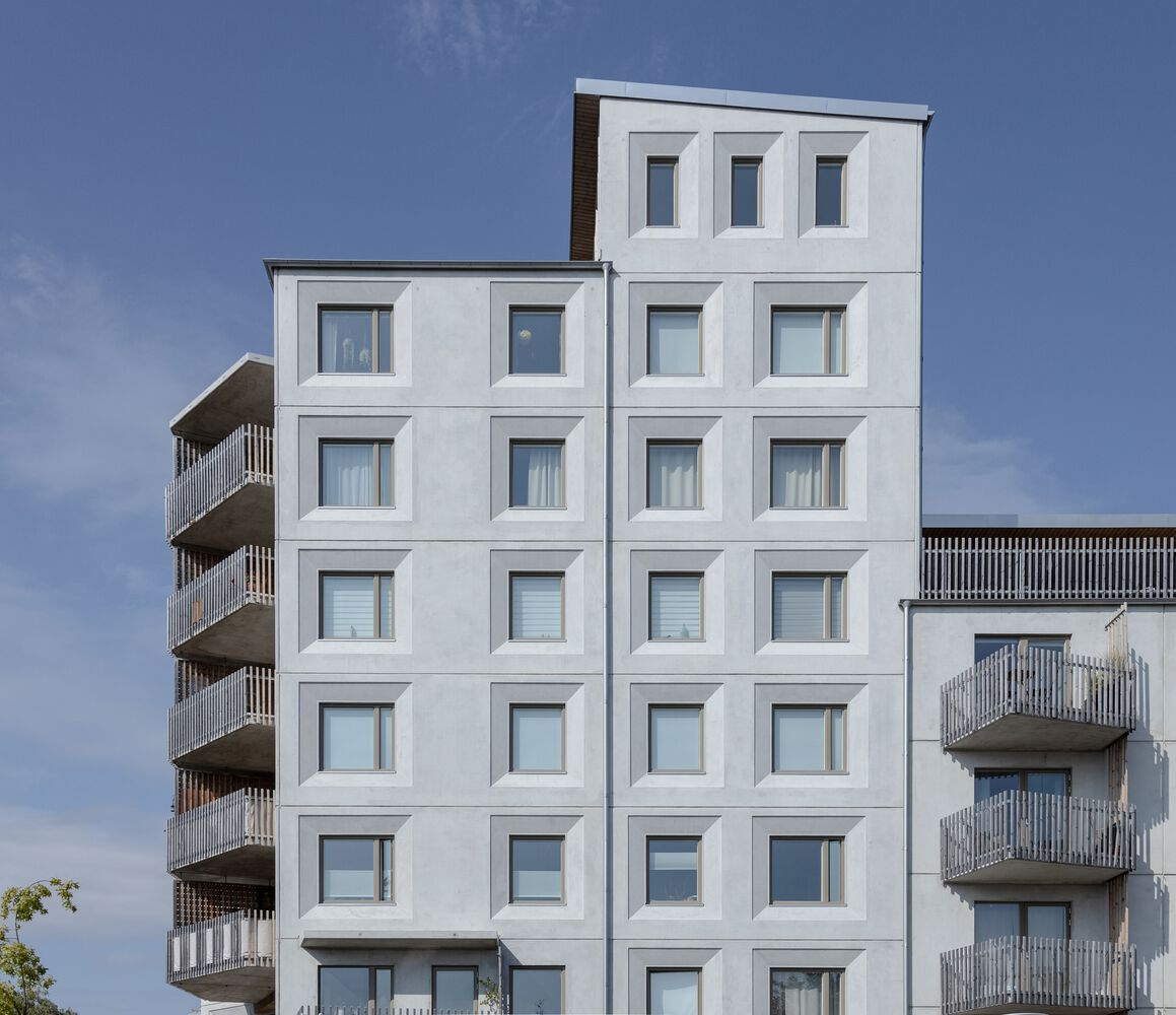 White facade with grid of framed windows flanked by balconies with vertical screening under blue sky