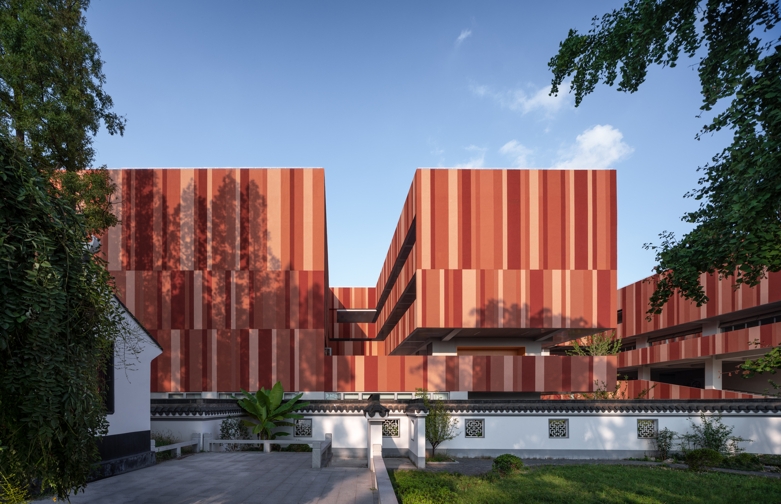 Striped terracotta panel facade rising above a white traditional perimeter wall with ornamental details