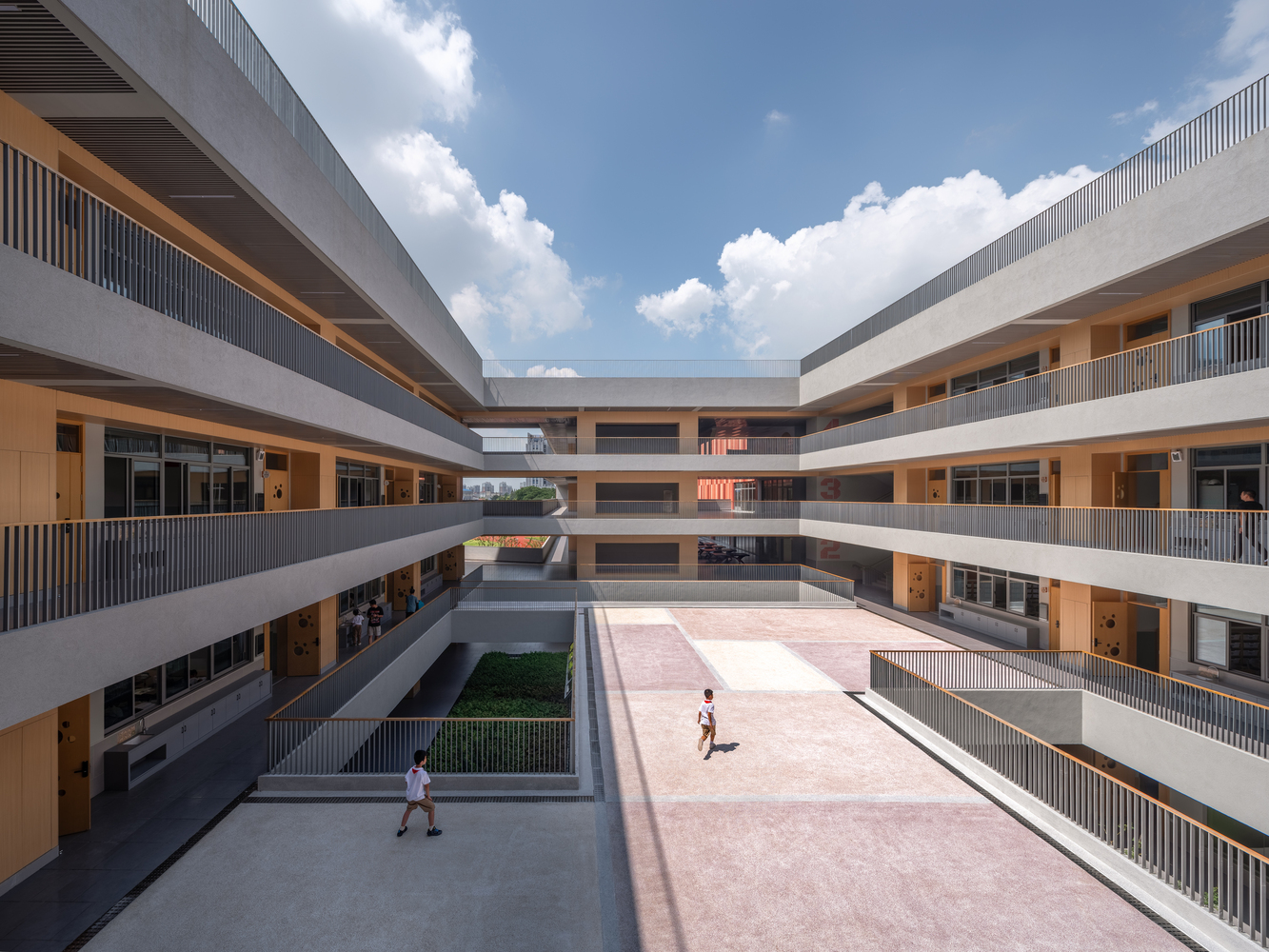 Courtyard view between concrete circulation galleries with timber screens and students crossing under afternoon clouds