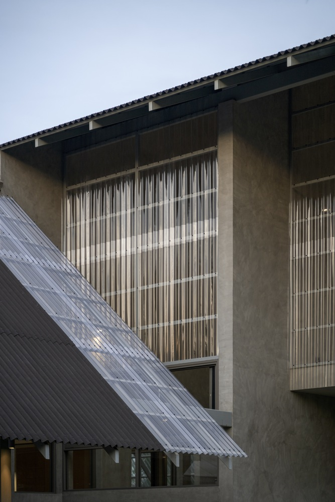Concrete facade with vertical louvered screens and a translucent corrugated canopy at dusk