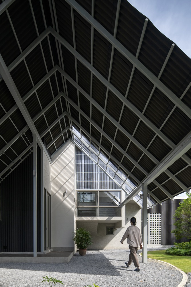 Concrete volumes with corrugated metal cladding beneath the triangular steel framework roof as a figure walks through