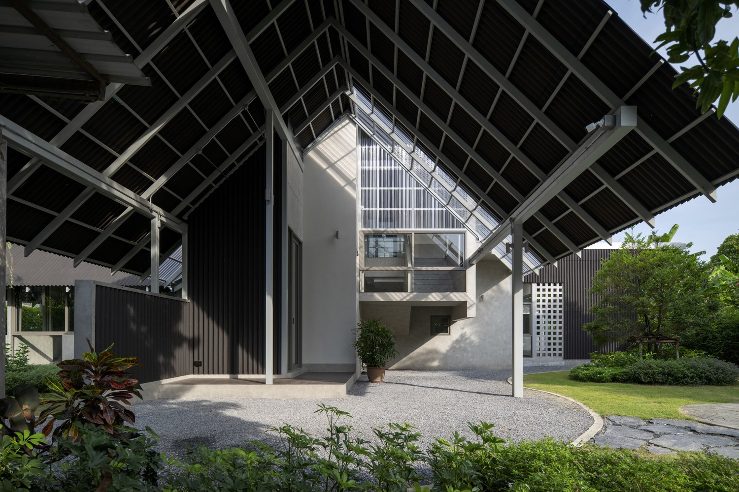 Entry plaza with gravel surface beneath the triangular pitched roof structure surrounded by potted plants