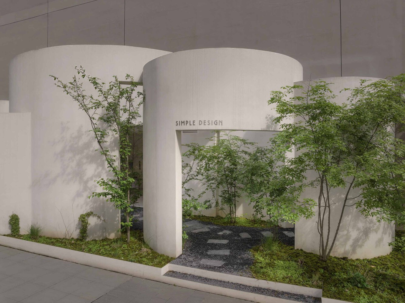 Arched entrance portal with cylindrical white walls framed by delicate trees and gravel courtyard