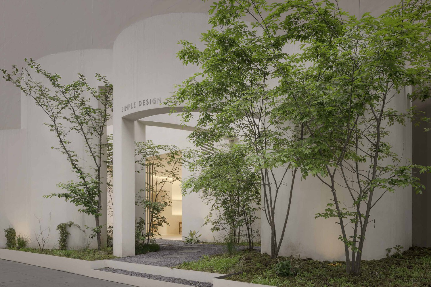 Entry courtyard with arched portico and slender maples casting shadows on gravel at twilight