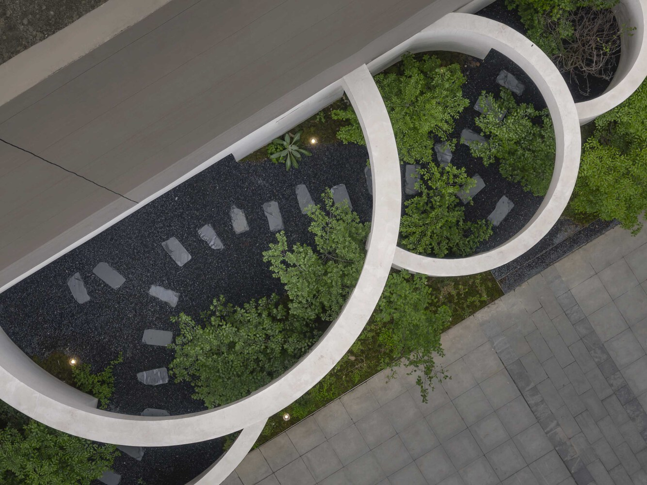 Aerial view of linked circular courtyard planters with dark gravel and green shrubs beside paved walkways