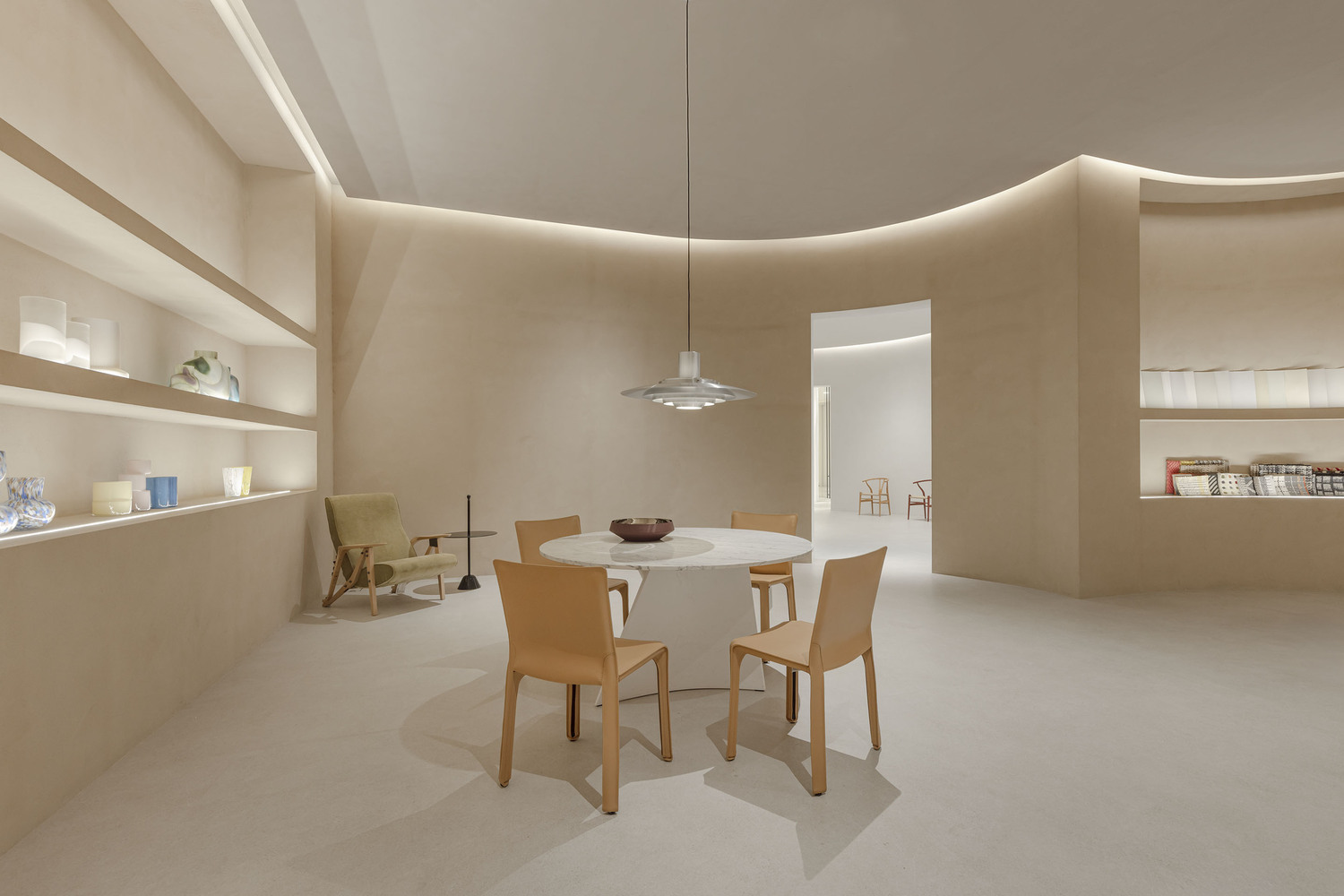 Interior gallery space with curved walls, recessed cove lighting, built-in display shelves and a round dining table