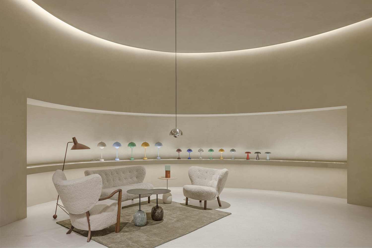 Curved exhibition room with horizontal display shelf holding colorful lamps and upholstered seating below