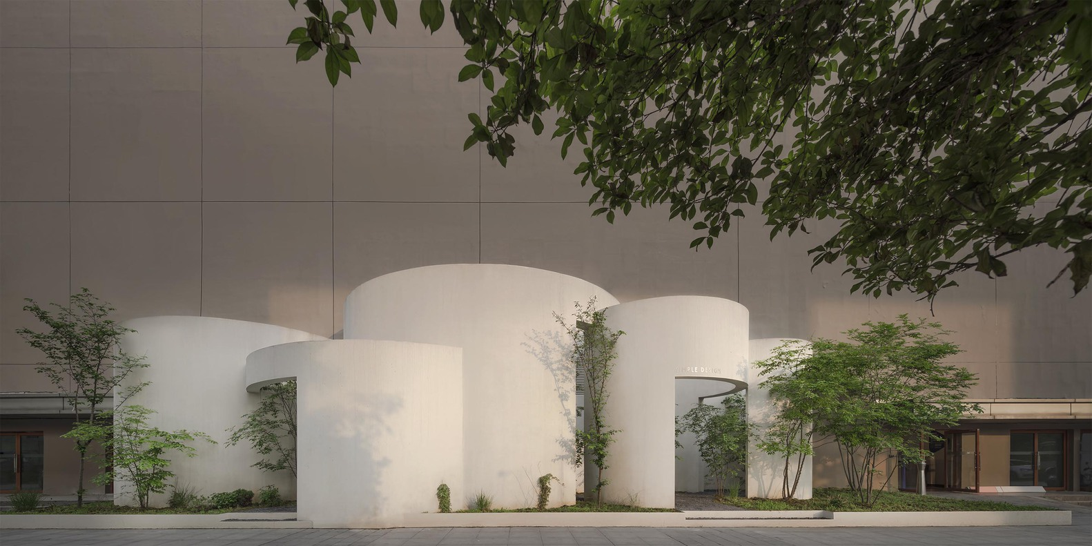 Street view of the white cylindrical facade with arched openings and trees at dusk