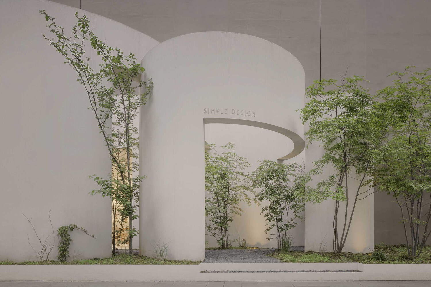 Curved entry portal in white plaster with spiral cut and flanking trees from sidewalk