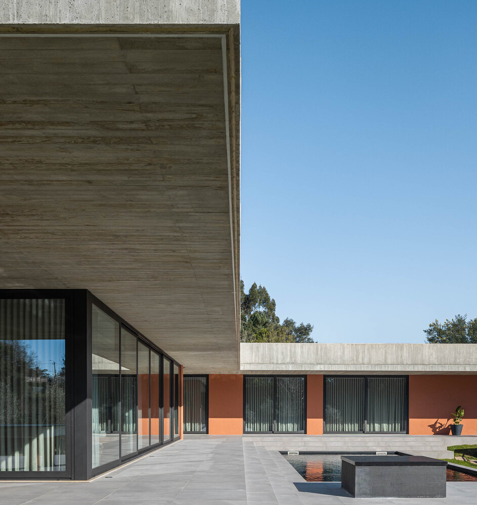 Courtyard view showing board-formed concrete volumes, orange stucco walls, and shallow reflecting pool under clear sky