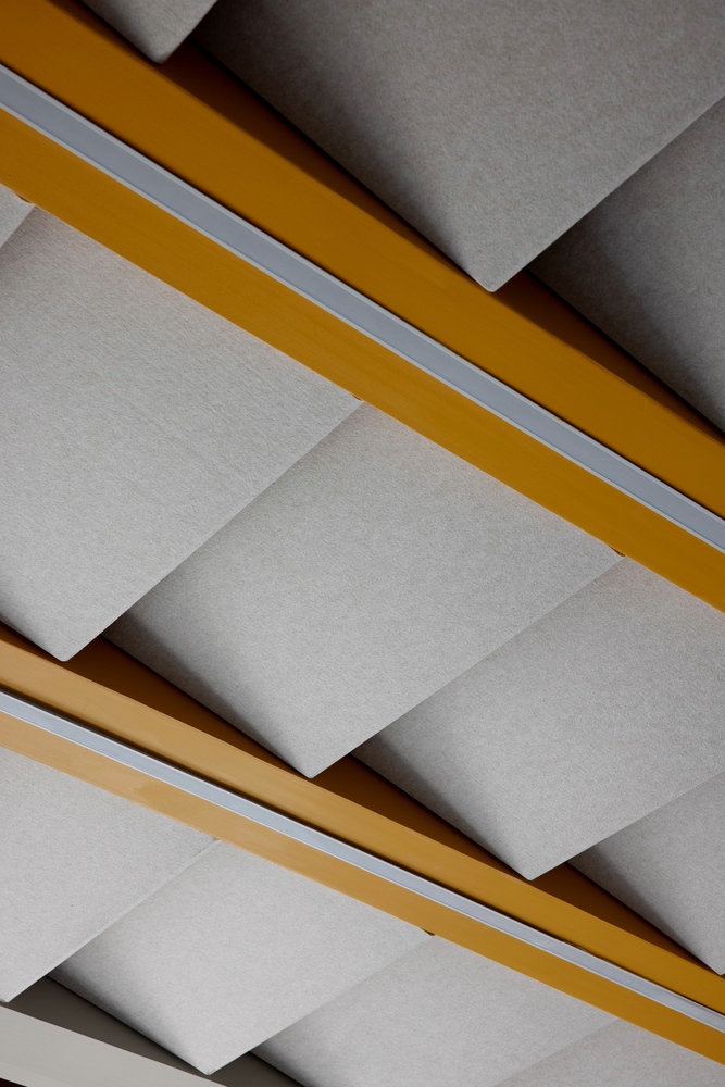 Ceiling detail showing white panels with yellow and tan timber beams casting angular shadows