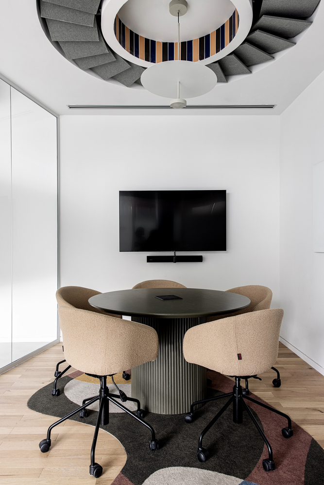 Small meeting room with circular opening revealing striped stairs and ceiling fan above