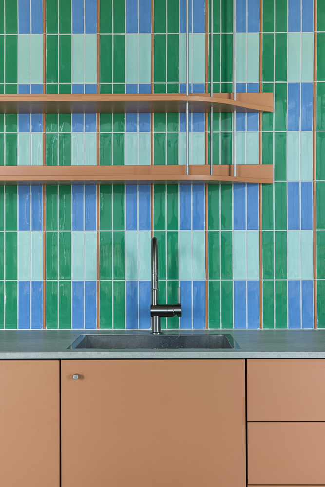 Kitchen backsplash with vertical stripe tiles in green and blue with timber shelves and tan cabinetry