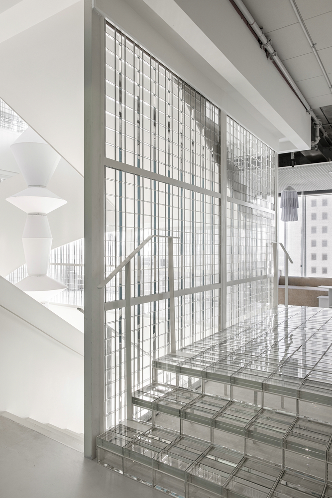 Glass block staircase ascending alongside a gridded translucent screen wall with white railing