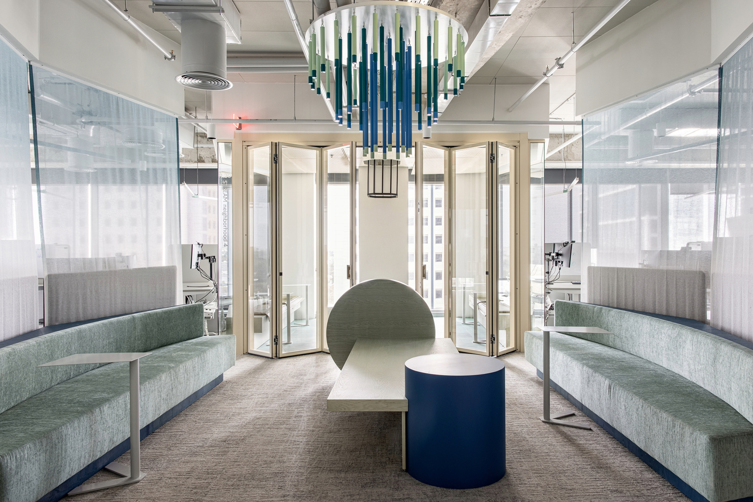 Lounge with green upholstered benches flanking a central table beneath a cascading glass chandelier