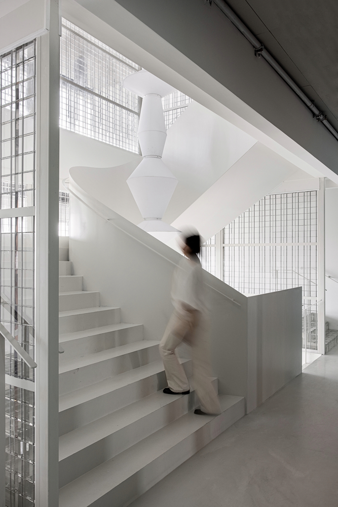 Central staircase with a figure in motion ascending the steps behind wire mesh partitions and white sculptural column overhead