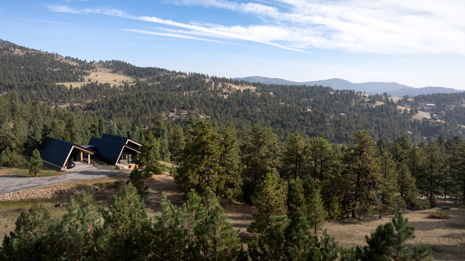 Distant view of the two pitched roofs nestled among pines on a sloping ridgeline