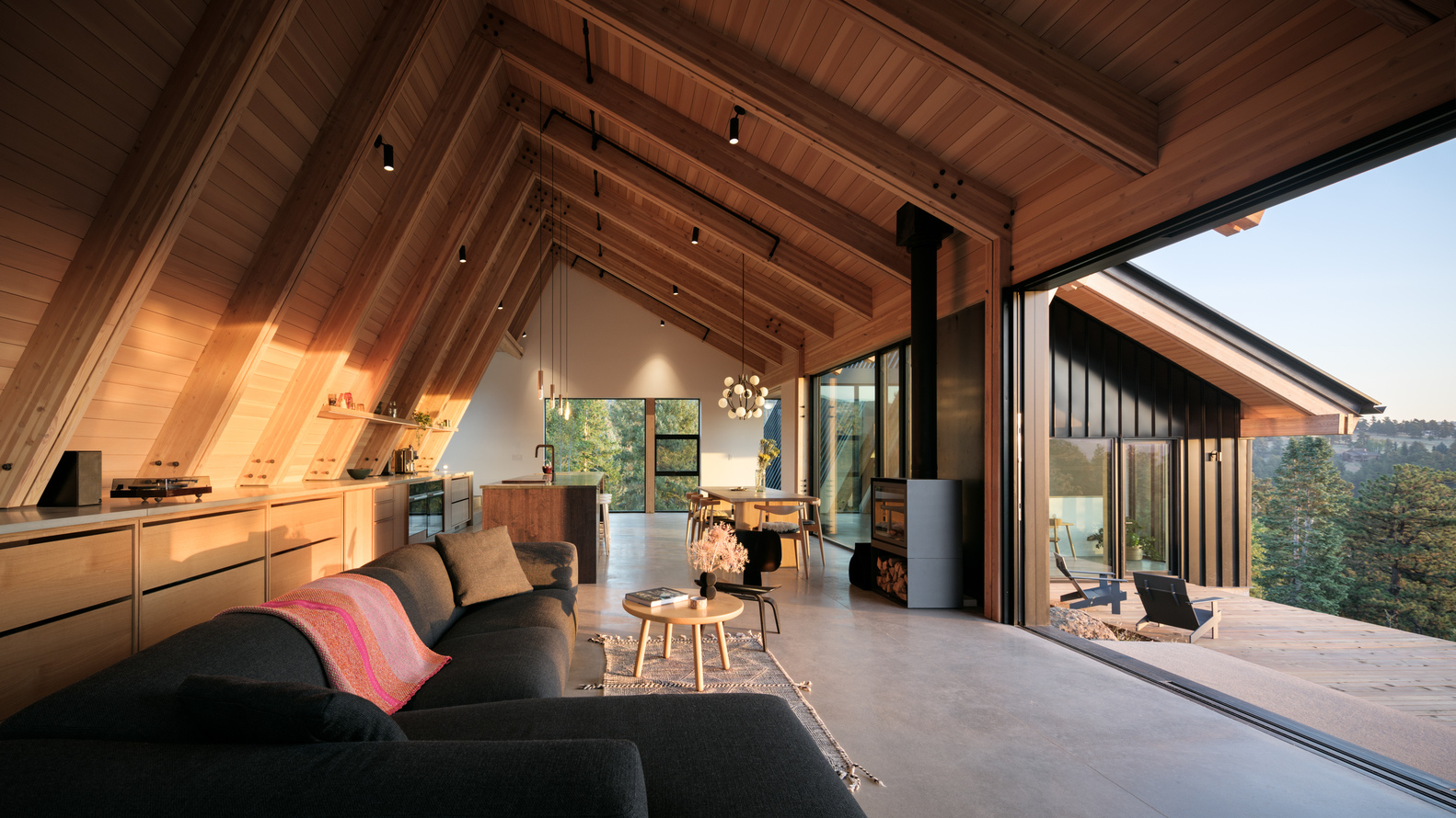 Open living space with exposed timber rafters and folding glass wall opening to terrace at dusk