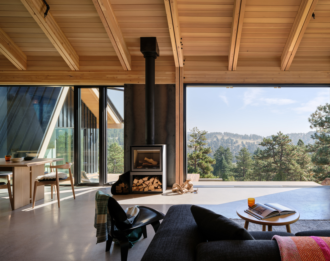 Living room with freestanding wood stove and panoramic opening framing forested hillside views