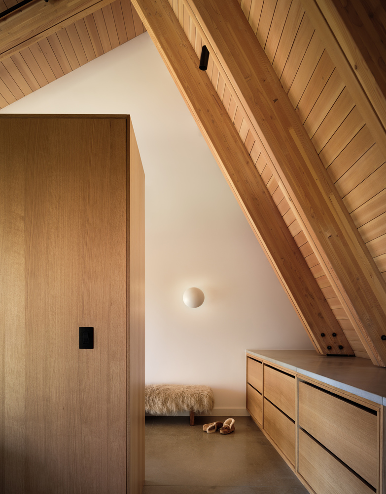Corner nook with timber door, angled ceiling beams, built-in bench, and circular wall sconce casting soft light