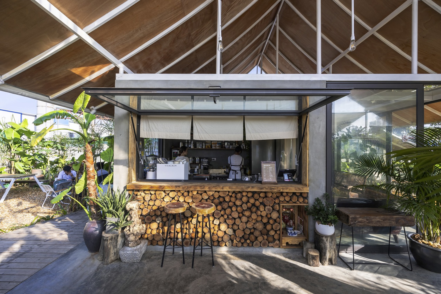 Outdoor cafe counter with stacked firewood base under an exposed timber rafter ceiling