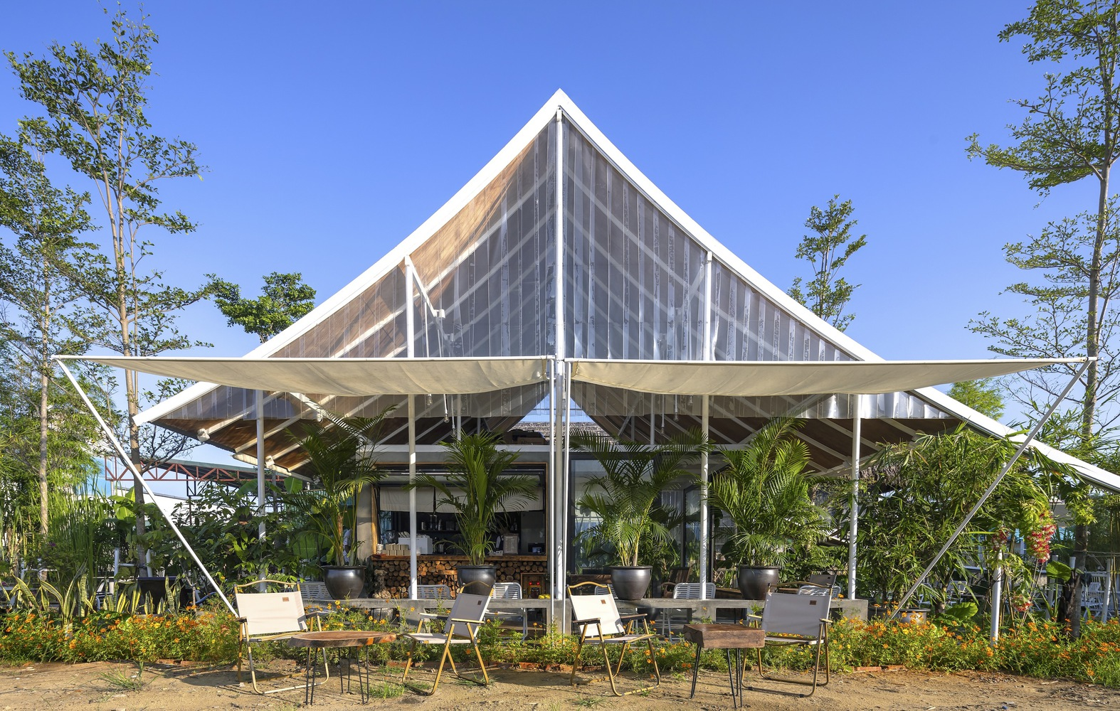 Gabled pavilion with tensile canopy wings and translucent walls surrounded by young trees