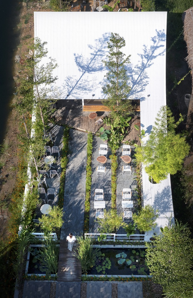 Top-down view of a white corrugated roof with tree shadows and a linear courtyard below