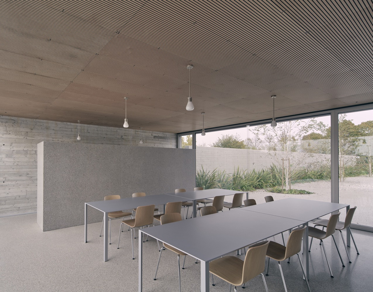 Dining room with timber slat ceiling and pendant lights overlooking planted courtyard through floor-to-ceiling glazing