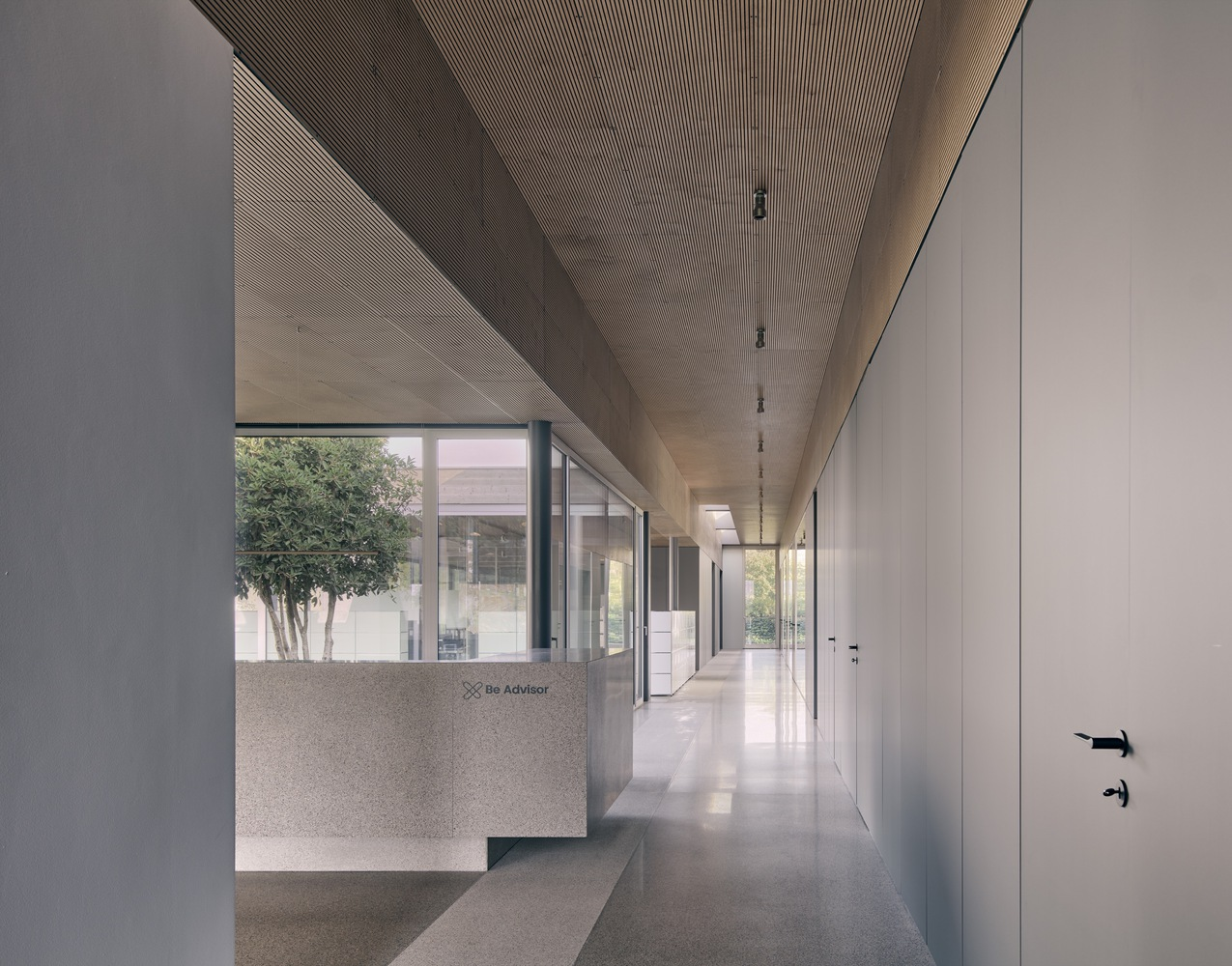 Corridor with grooved timber ceiling and terrazzo reception desk overlooking a planted courtyard