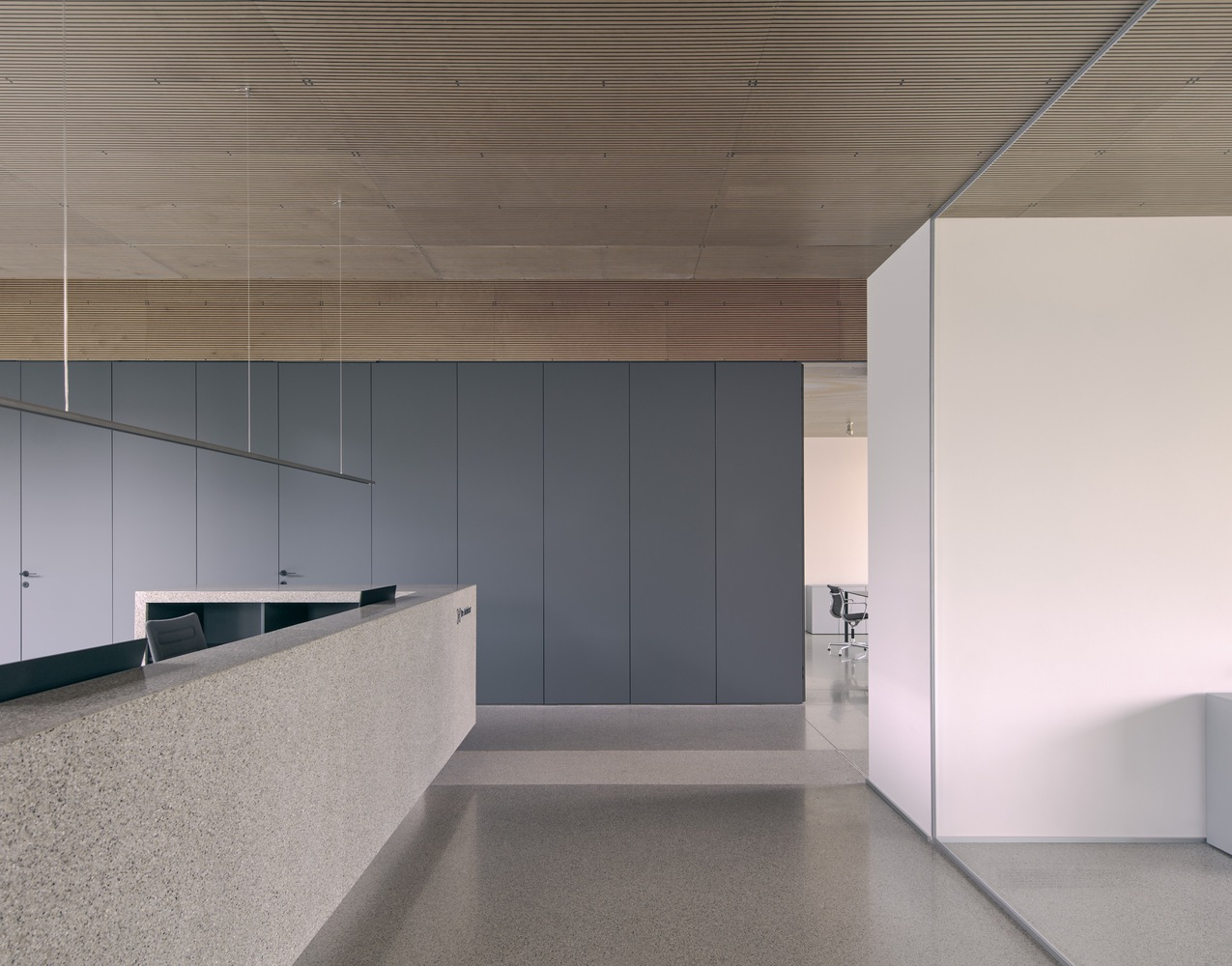 Reception area with terrazzo desk and grey paneled storage wall beneath a timber-lined ceiling